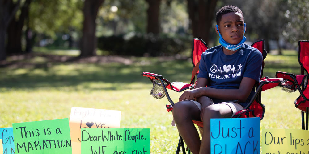 Zyon Thorpe is surrounded by signs in support of Ahmaud Arbery outside of the Glynn County Courthouse during a rally on Oct. 16.