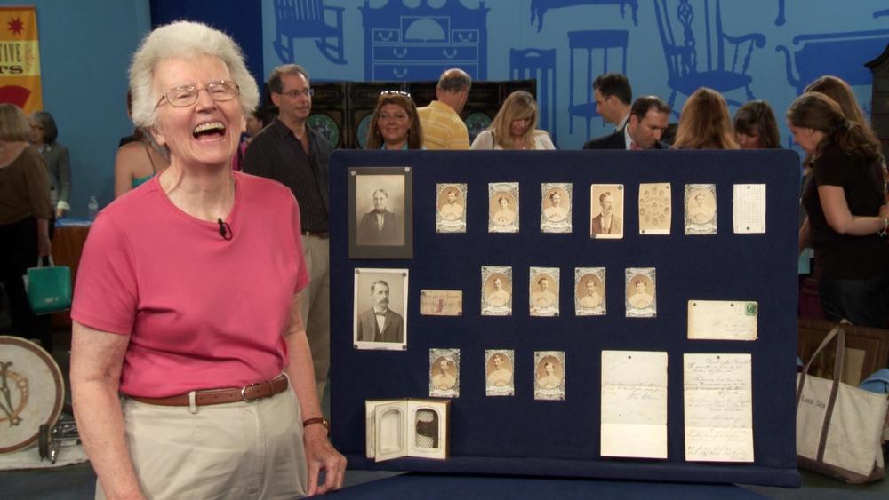 A woman laughs in front of a collection of baseball cards being appraised.