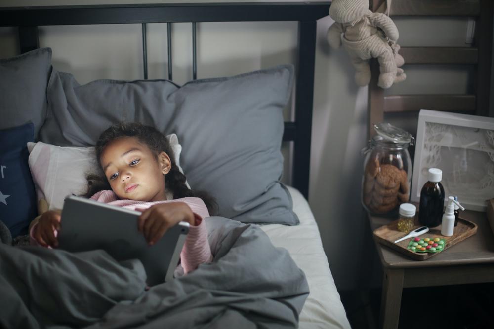A girl looks at a screen in bed.