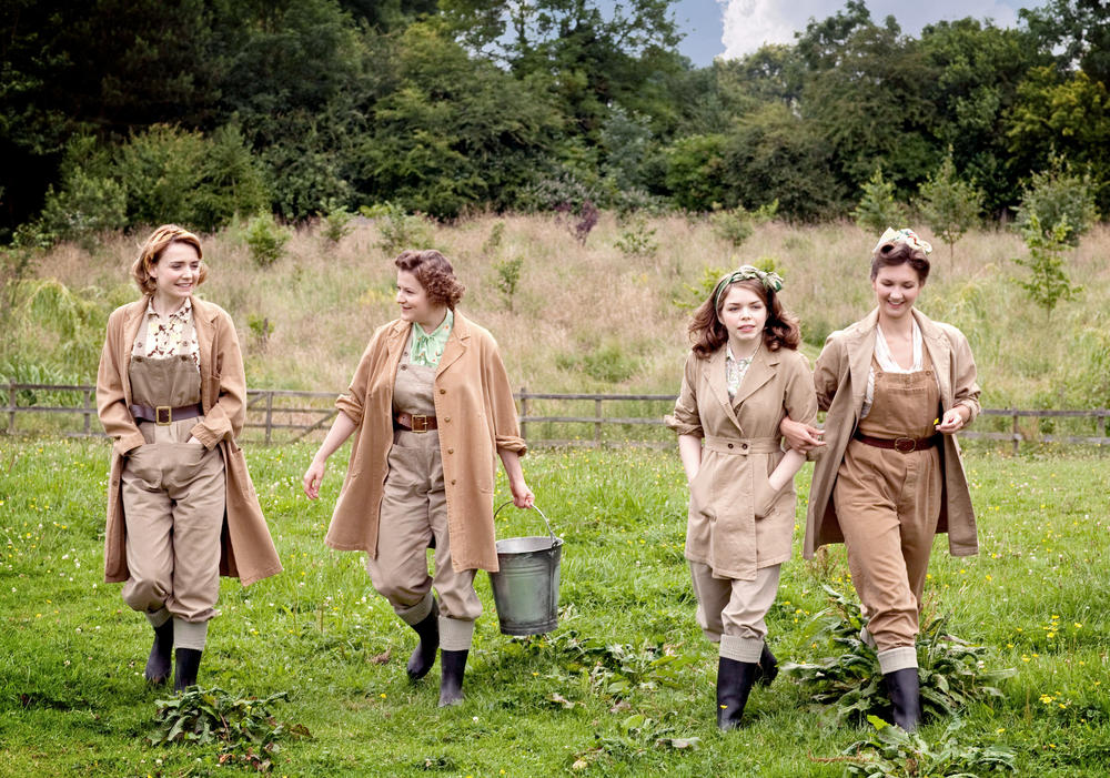 4 women walking through a field in period farm clothing.