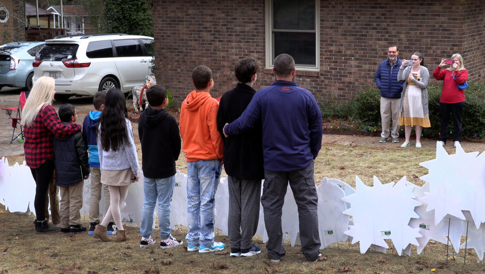 Standing behind a sign that reads “It’s Adoption Day,” Angela and Elliott Turbeville pose for a family photograph with the six children they adopted Monday. The Turbevilles surprised the children on Dec. 20 with the news they would be going to court that afternoon to finalize the adoption. 12/20/2021