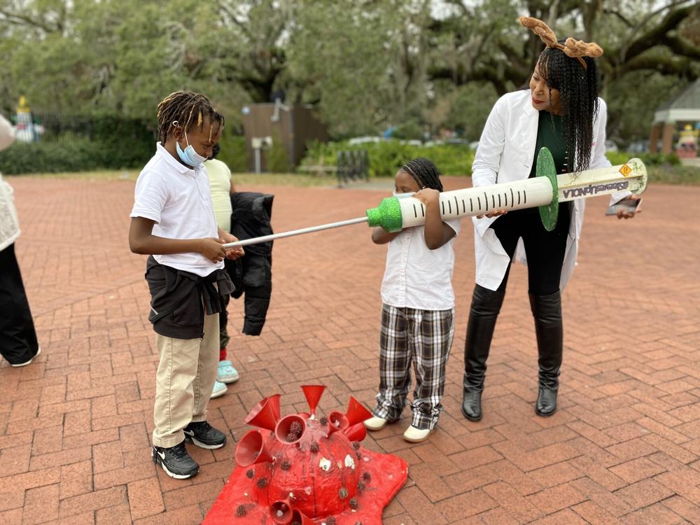Cali Bell pretends to give her brother Calvin Bell a giant COVID-19 shot at a vaccine clinic in New Orleans, with some help from Louisiana Region One medical director Shantel Hébert-Magee.