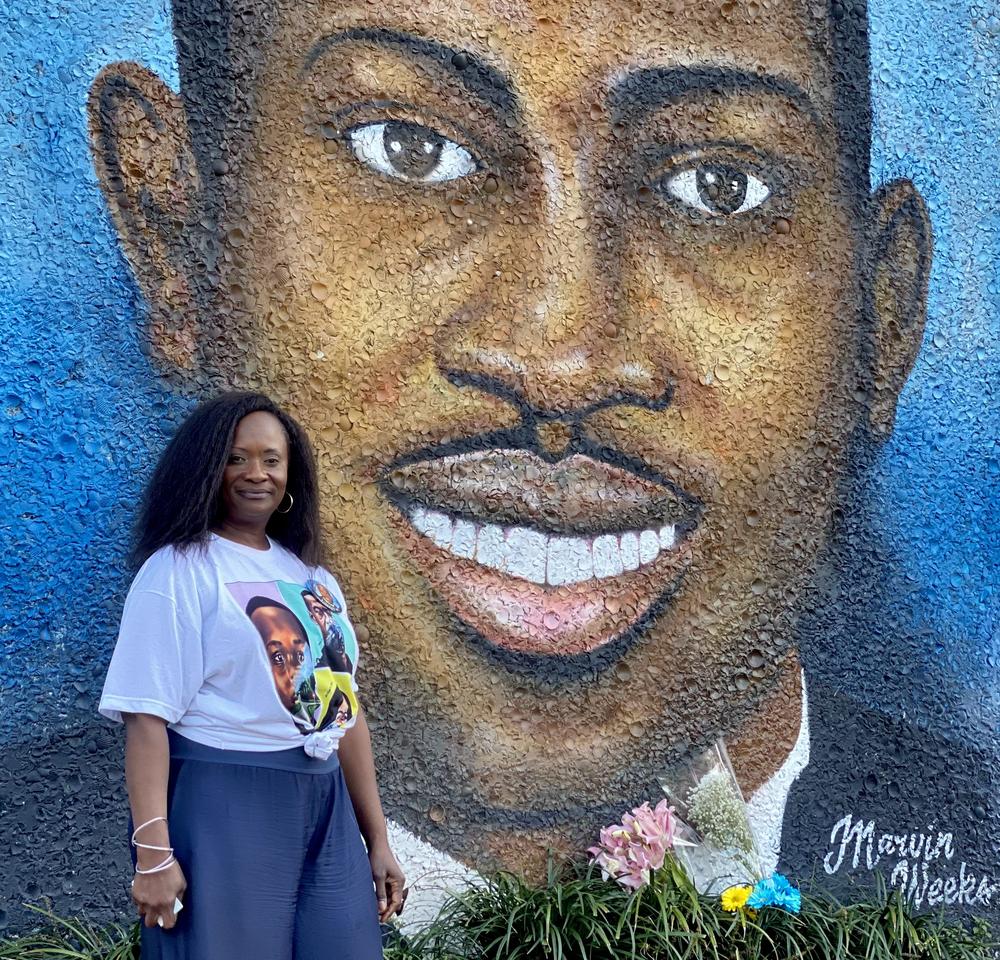 Brunswick resident Dana Roberts Beckham poses next to a mural of Ahmaud Arbery on the side of a building in Brunswick. In the mural, Arbery is wearing a black tuxedo and a white collared shirt.
