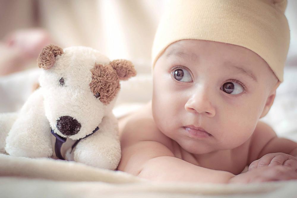 infant on belly next to plush dog