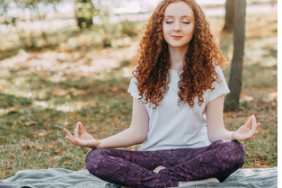 A woman with long, red, curly hair sits with closed eyes and hands in meditative position