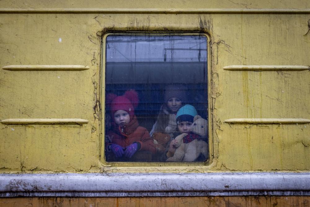 Children Vlada, left, Katrin and Danilo look out from a window of an unheated train carriage of an emergency evacuation train which is travelling from Kharkov to Lviv, as it stopped in the Kyiv railway station in Kyiv, Ukraine, Thursday, March 3, 2022.