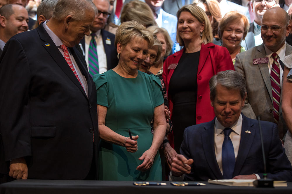 Governor Kemp signs bill while Speaker Ralston and his wife Sheree look on.