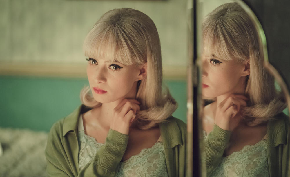 A young woman stares at her reflection in a mirror.