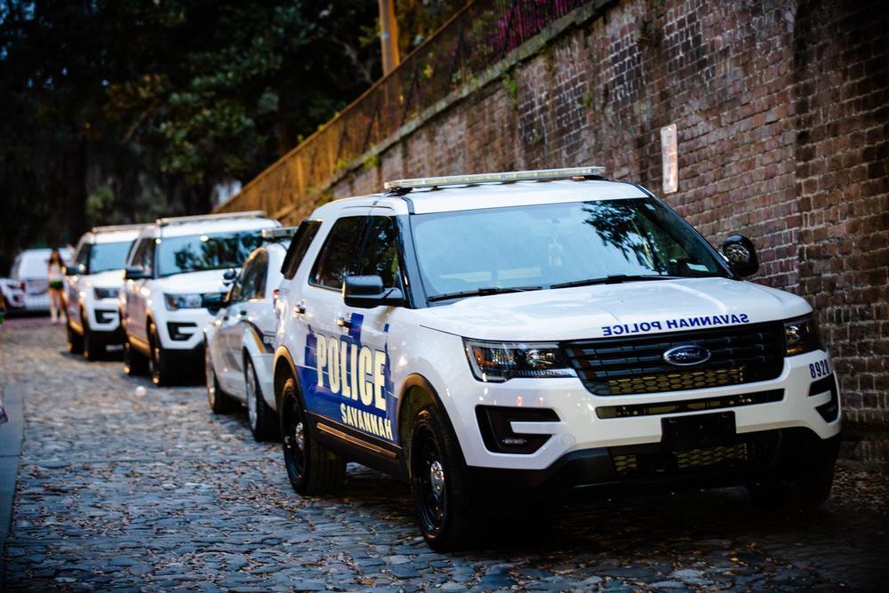 Four Savannah Police Department squad cars are parked in front of one another on a brick road.