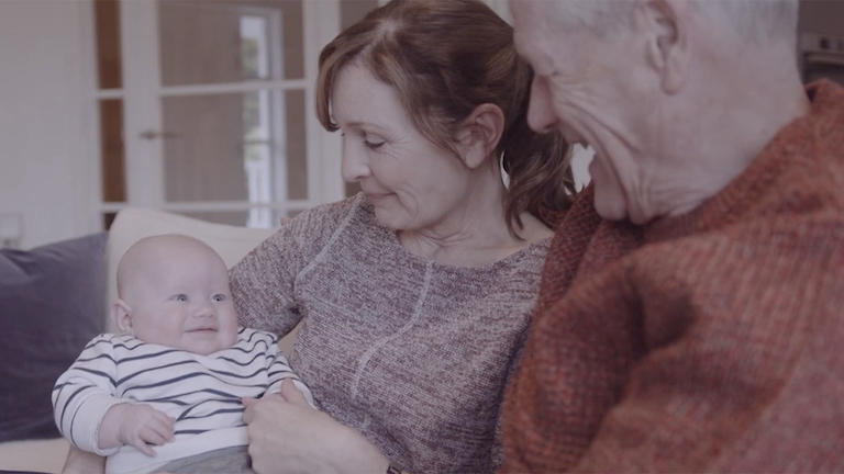 A couple holds their smiling grandchild.