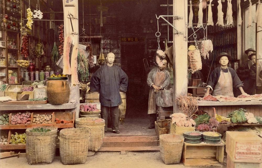 A butcher displays hanging meats, fruits and vegetables at his grocery shop in San Francisco’s Chinatown, 1887.