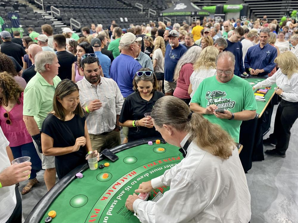 A group of people is standing around a blackjack table at Enmarket Arena, waiting for the dealer to shuffle cards.