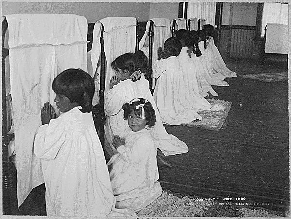  Unidentified Native American girls at the Phoenix Indian School in June 1900 pray beside their beds.