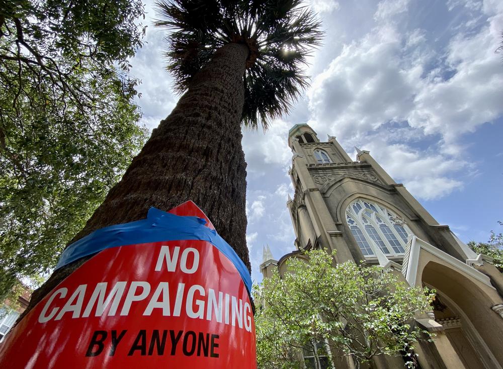 A bright red sign that reads "no campaigning" is taped around a palm tree across the street from the synagogue of Congregation Mickve Israel in downtown Savannah.