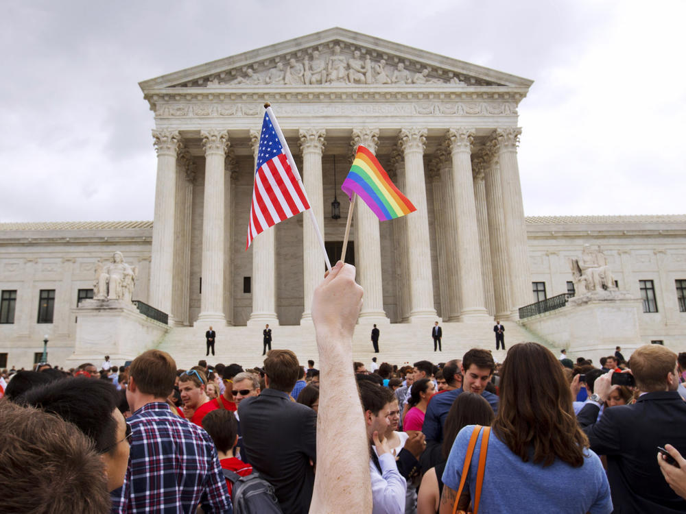 In this June 26, 2015 file photo, a man holds a U.S. and a rainbow flag outside the Supreme Court in Washington after the court legalized gay marriage nationwide. Court documents show the state of Alaska for years maintains a discriminatory policy that denied some same-sex spouses benefits by wrongly claiming gay marriage was not recognized in Alaska, long after courts ordered they be recognized.