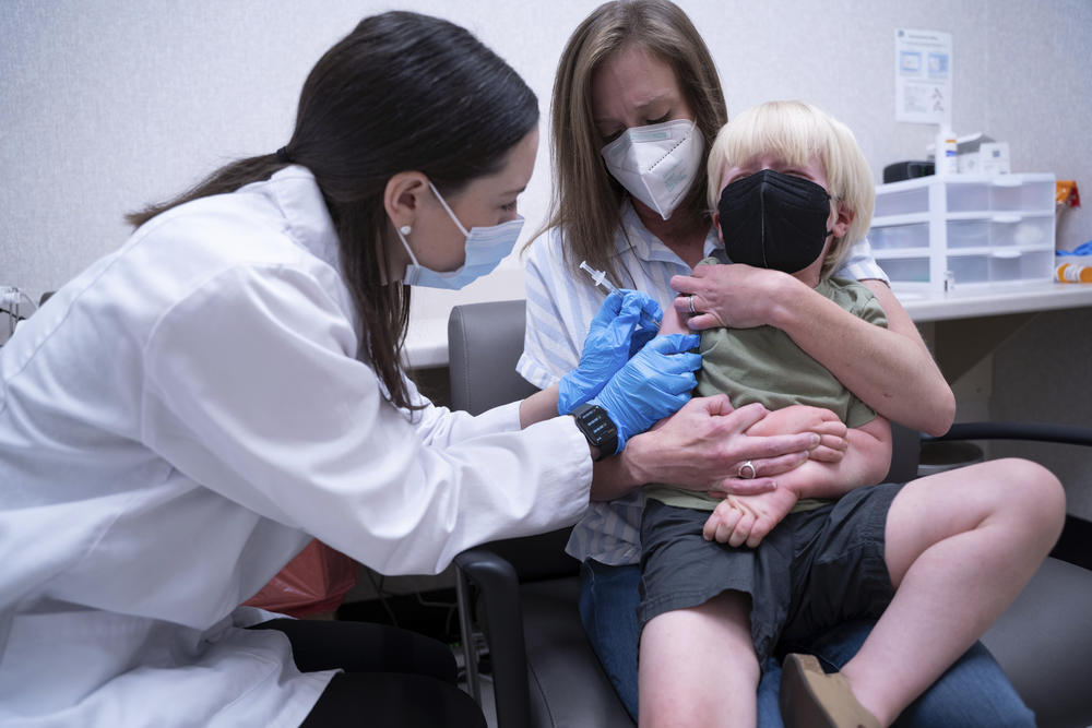 Pharmacist Kaitlin Harring, left, administers a Moderna COVID-19 vaccination to 3-year-old Fletcher Pack while he sits on the lap of his mother, McKenzie Pack, at Walgreens pharmacy Monday, June 20, 2022, in Lexington, S.C. COVID-19 vaccinations are now available to children under 5 in the United States. (AP Photo/Sean Rayford)