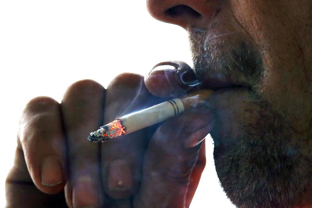 A closeup of a person's nose, mouth and hand while smoking a cigarette