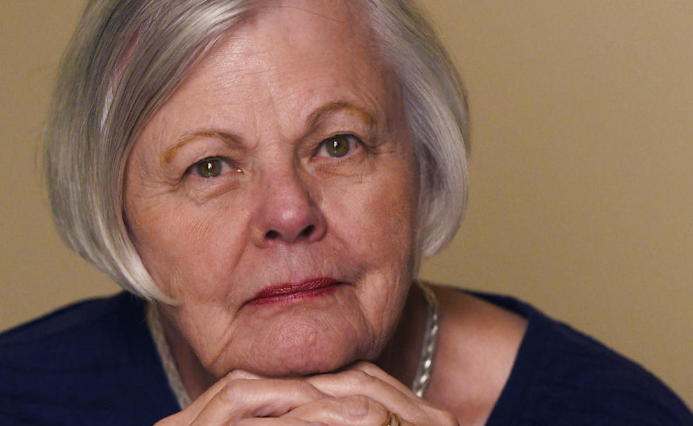 a closeup of silver-haired woman's face with hands folded under her chin