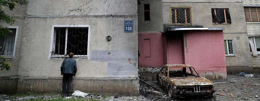 A man looks though the window of a destroyed building.