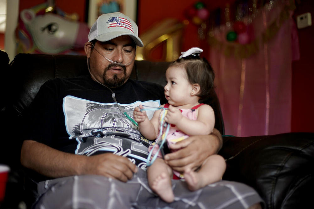 A man holds his 8-month-old daughter while on oxygen