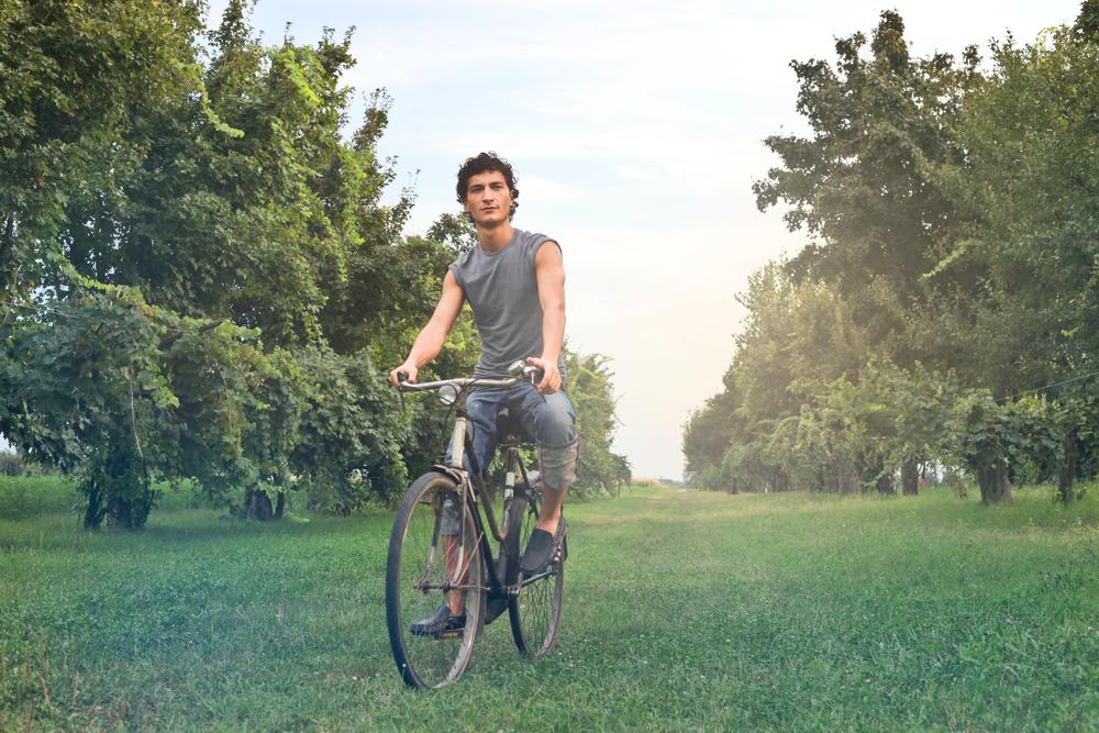 Man in grey t-shirt rides a bicycle through a grassy field.