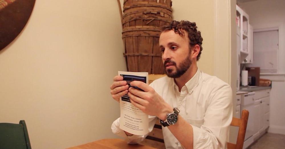 A man sits at a table holding a book.