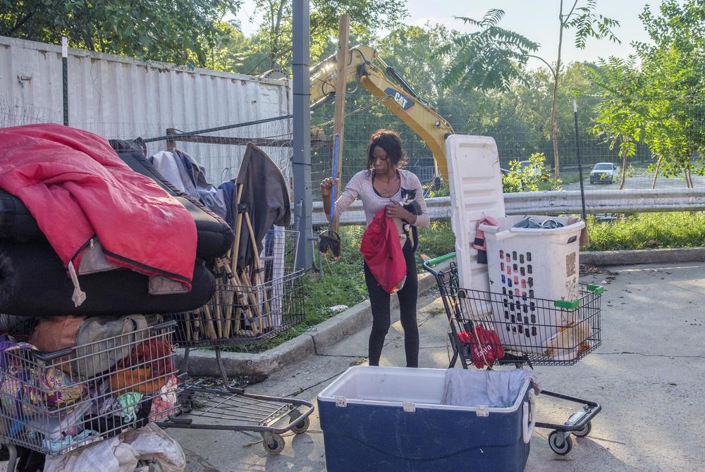 Tonithia Fernandez holds one of her two cats while also trying to pack up and move her home as a Macon-Bibb County excavator clears out another part of the encampment where she lived until Tuesday.