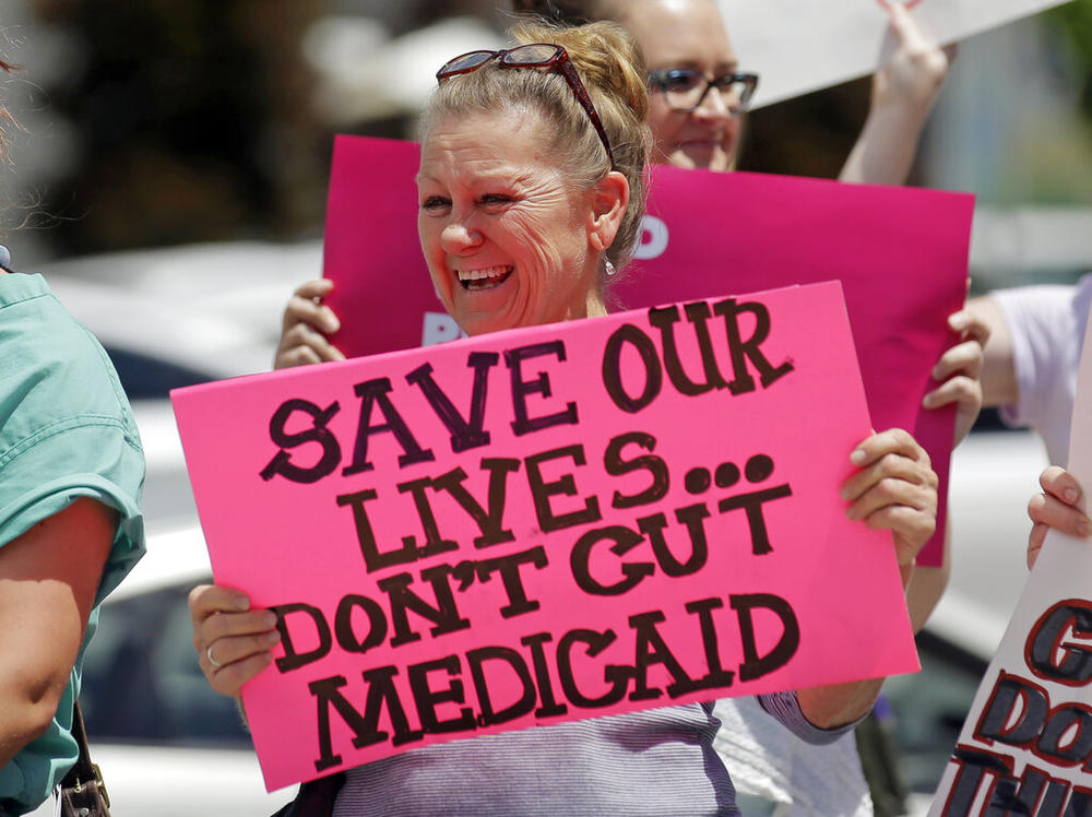 A woman holds a pink signs that says, "save our lilves ... don't gut medicaid"