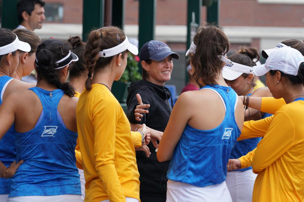 A smiling coach Amy Bryant is surrounded by Emory student athletes.