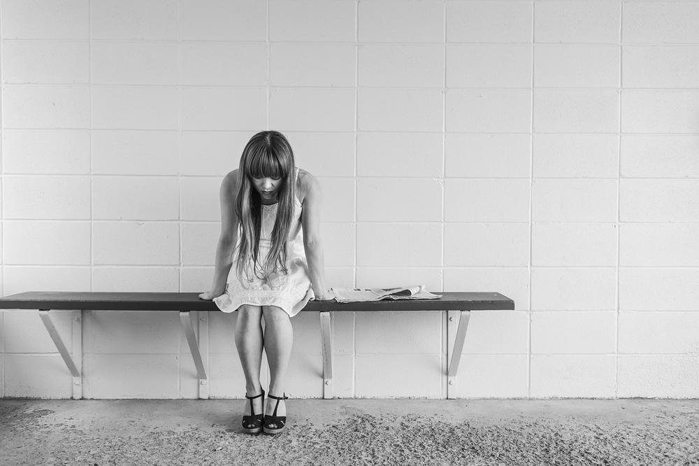 A worried young woman sits on a bench in this stock image.