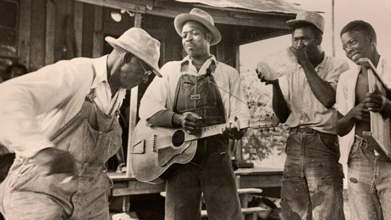 Four musicians play and dance in an old photograph.