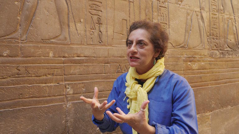 A woman stands in front of a wall of hieroglyphics.