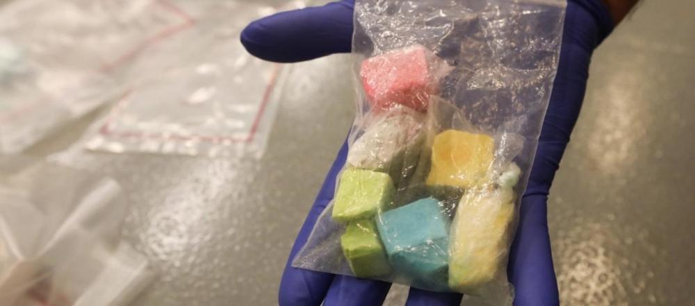 A gloved hand holding a bag of colored fentanyl candy.