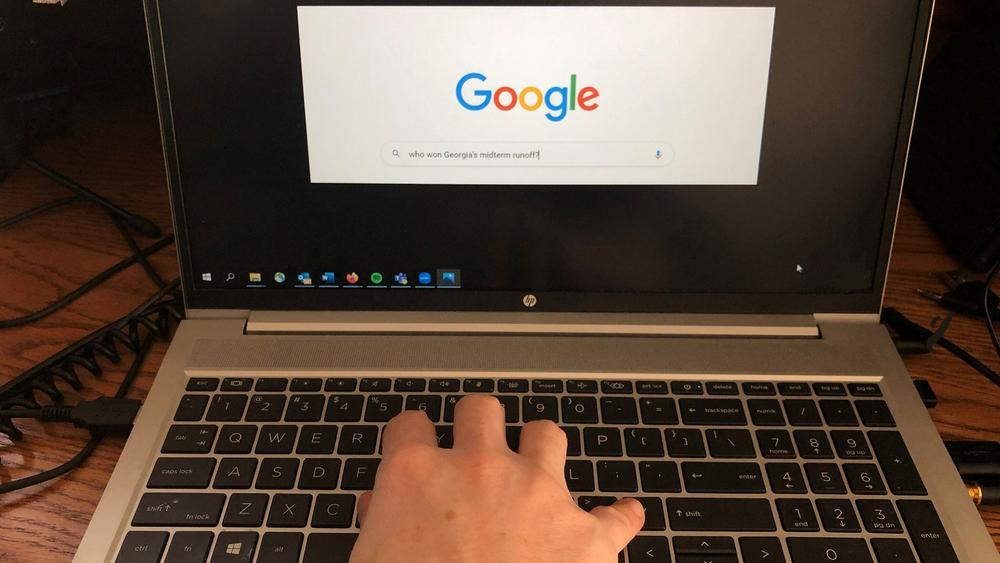 A hand types a search query on Google