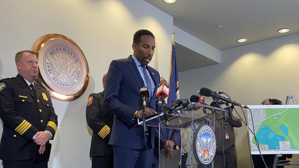 Atlanta Mayor Andre Dickens is shown standing behind a podium and speaking into microphones, flanked by police officials.