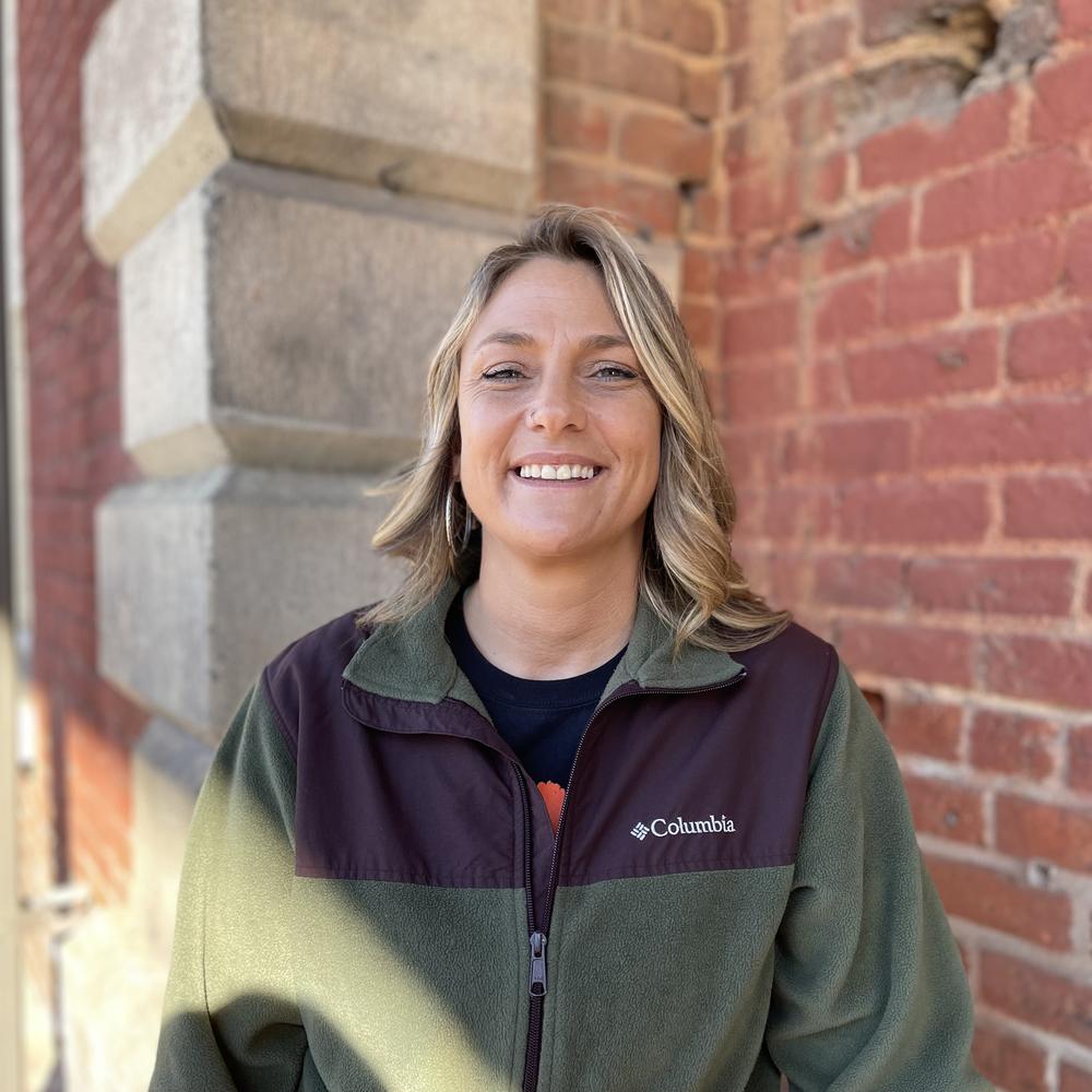 Amanda Williamson stands in front of a brick wall outside the Freight Depot