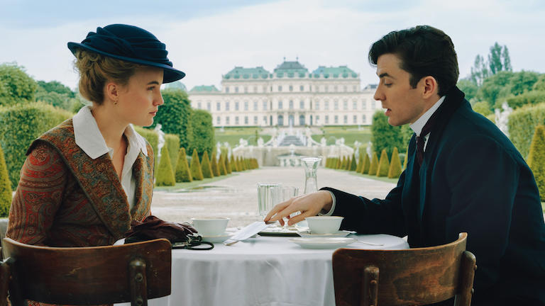 A man and woman in period dress sitting at a table outdoors.