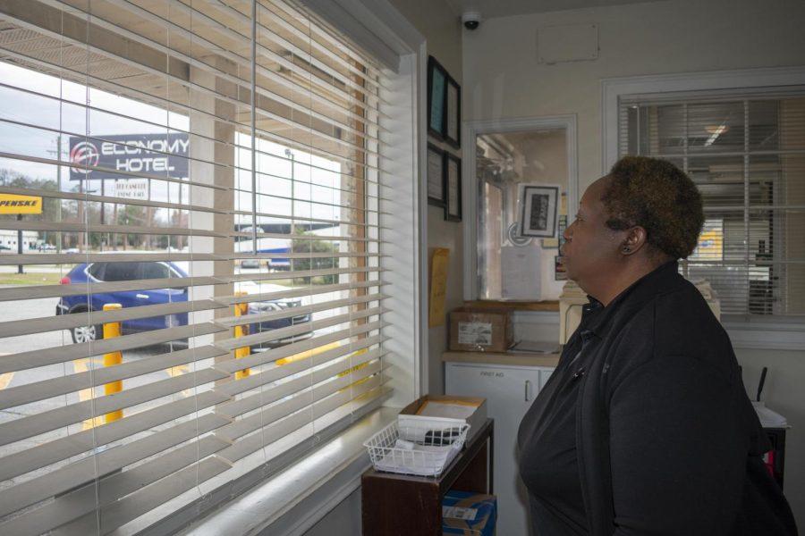 Laura Corley | The Macon Newsroom  Imogene Patterson peers through the blinds behind the check-in desk at Economy Hotel on Pio Nono. She said she sometimes holds her breath watching some of the hotel guests trying to cross the five lanes of Pio Nono Avenue to get to the Circle K convenience store.