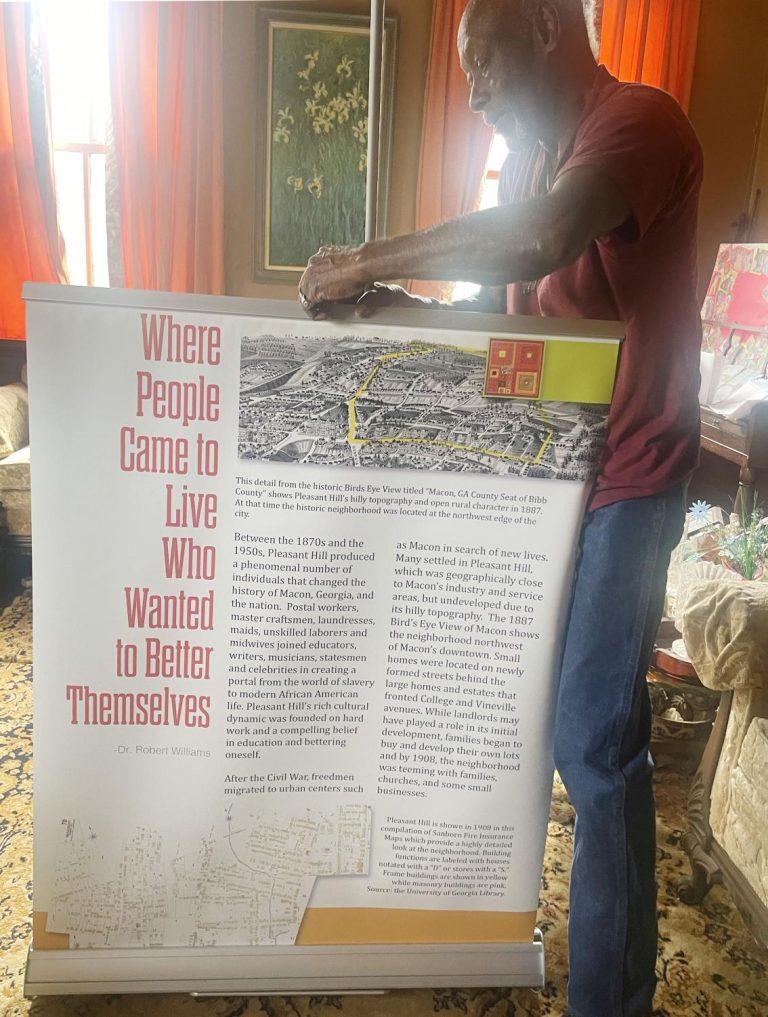Peter Givens unfurls part of a traveling exhibit of Pleasant Hill’s history in his living room. (Laura Corley | The Macon Newsroom)