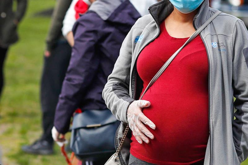 A pregnant woman holds her belly while waiting in line for groceries with hundreds at a food pantry.