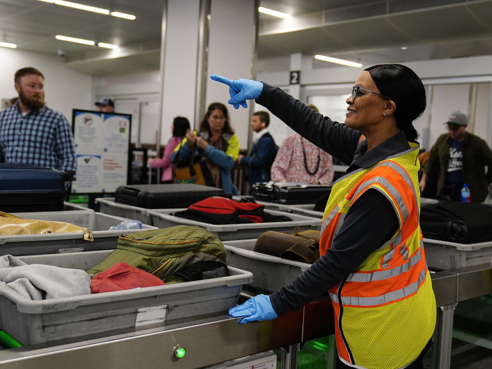 A worker points as people wait for the belongings at the Transportation Security Administration security area at the Hartsfield-Jackson Atlanta International Airport on Wednesday, Jan. 25, 2023, in Atlanta.