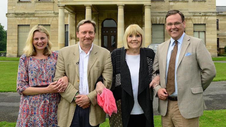 Four people standing in front of a manor with locked arms smiling.