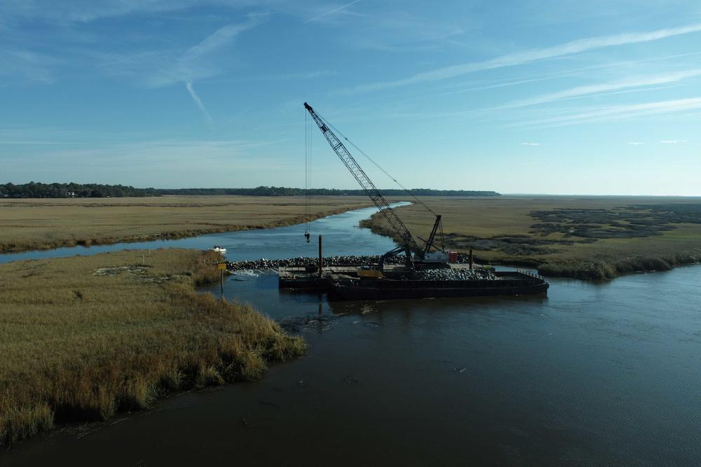 Two rivers are shown in an aerial view with heavy construction equipment floating on the water.