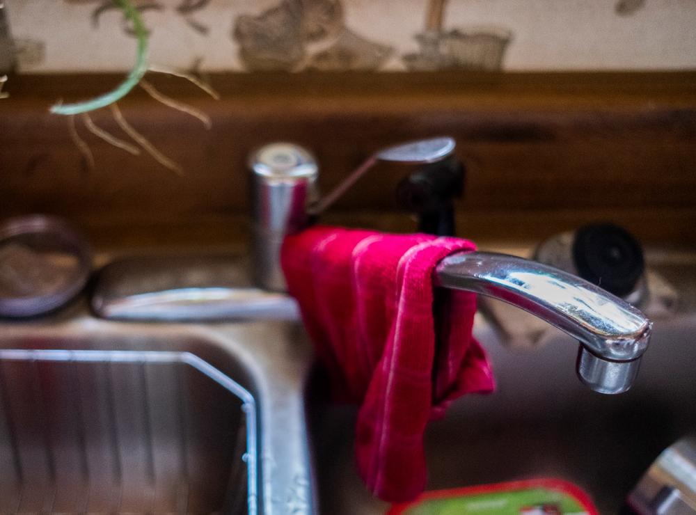 A kitchen sink's water faucet is shown with a rag hanging over it.