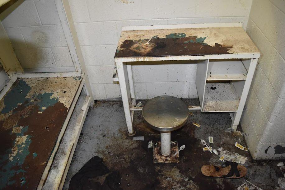 A dirty jail cell with trash strewn on the floor.