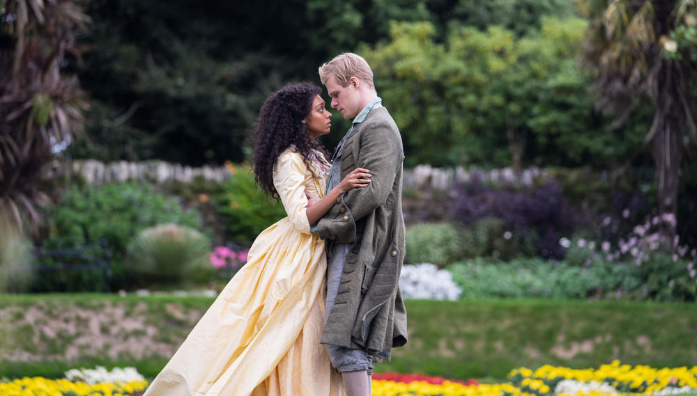 A young man and woman embrace in period dress.