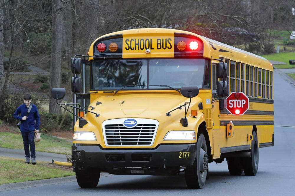 A child walks toward a yellow school bus stopped in a residential street.