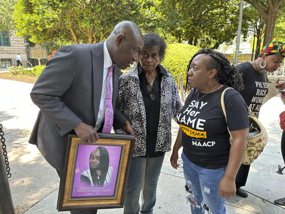 An attorney holding a picture of a young woman is shown talking with two women.
