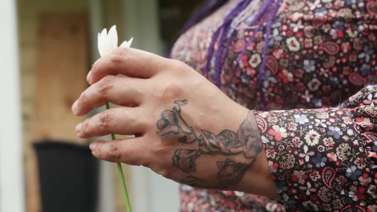 A tattooed hand holding a flower.