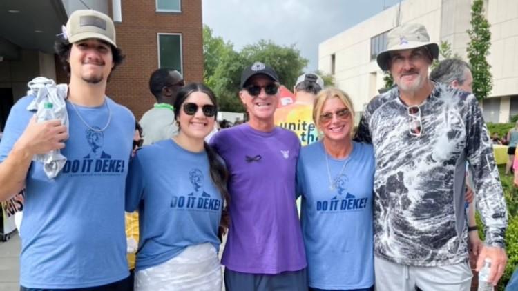 Five people are shown posing for a photo in T-shirts during a walk for cancer research.